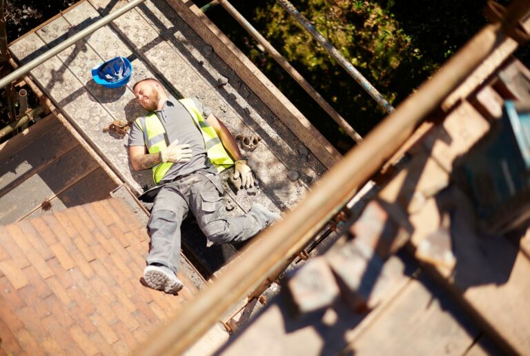 Ein abgestürzter, verletzter Bauarbeiter der auf einem Baugerüst auf einer Baustelle liegt.