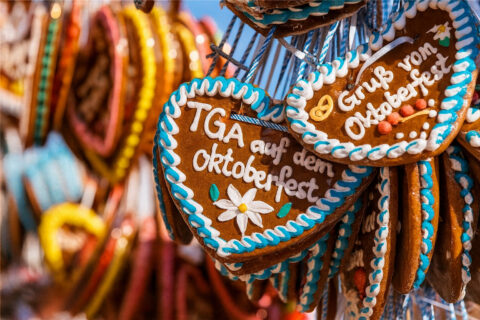 Ein Foto von Lebkuchenherzen, die auf dem Oktoberfest an einem Stand hängen. Das Lebkuchenherz im Vordergrund trägt die Aufschrift: TGA auf dem Oktoberfest. Die Lebkuchenherzen sind typisch für das Oktoberfest dekoriert.