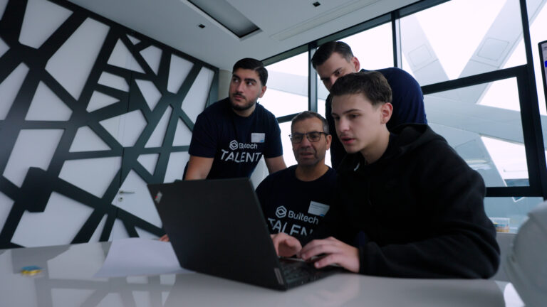 Älterer Azubi und jüngere Kollegen schauen gemeinsam auf den PC.