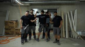 Eine Gruppe von Azubis der Firma elektroNWS ist abgebildet. Sie stehen in einer Tiefgarage beieinander und lächeln, während sie auf einen Azubi in der Mitte zeigen.